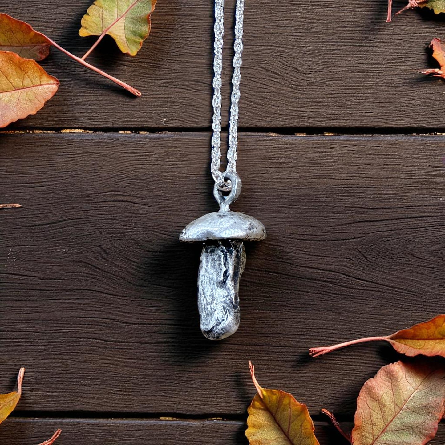Mushroom-shaped pendant necklace on a wooden surface with autumn leaves