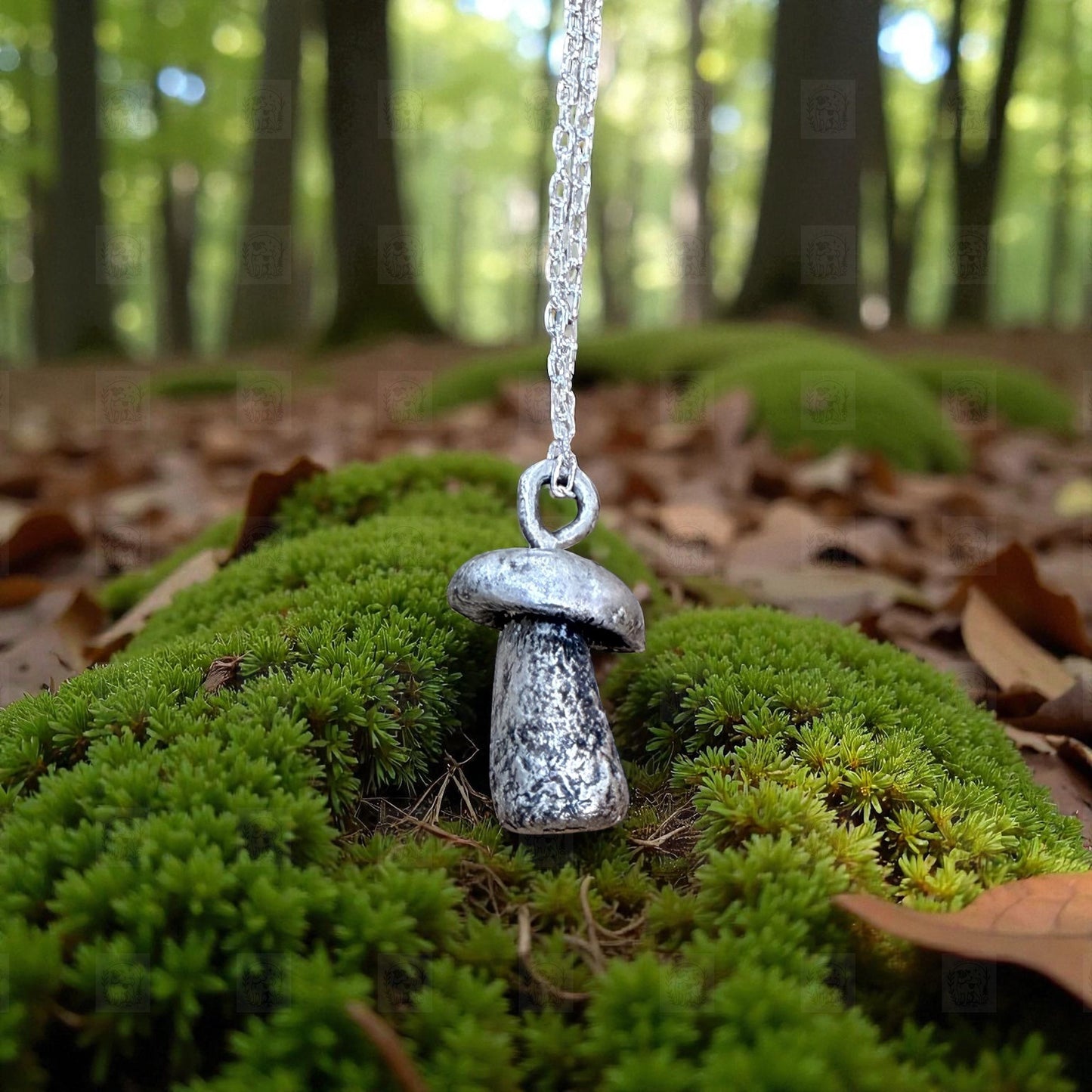 Silver mushroom-shaped pendant on a chain hanging over green moss in a forest setting.