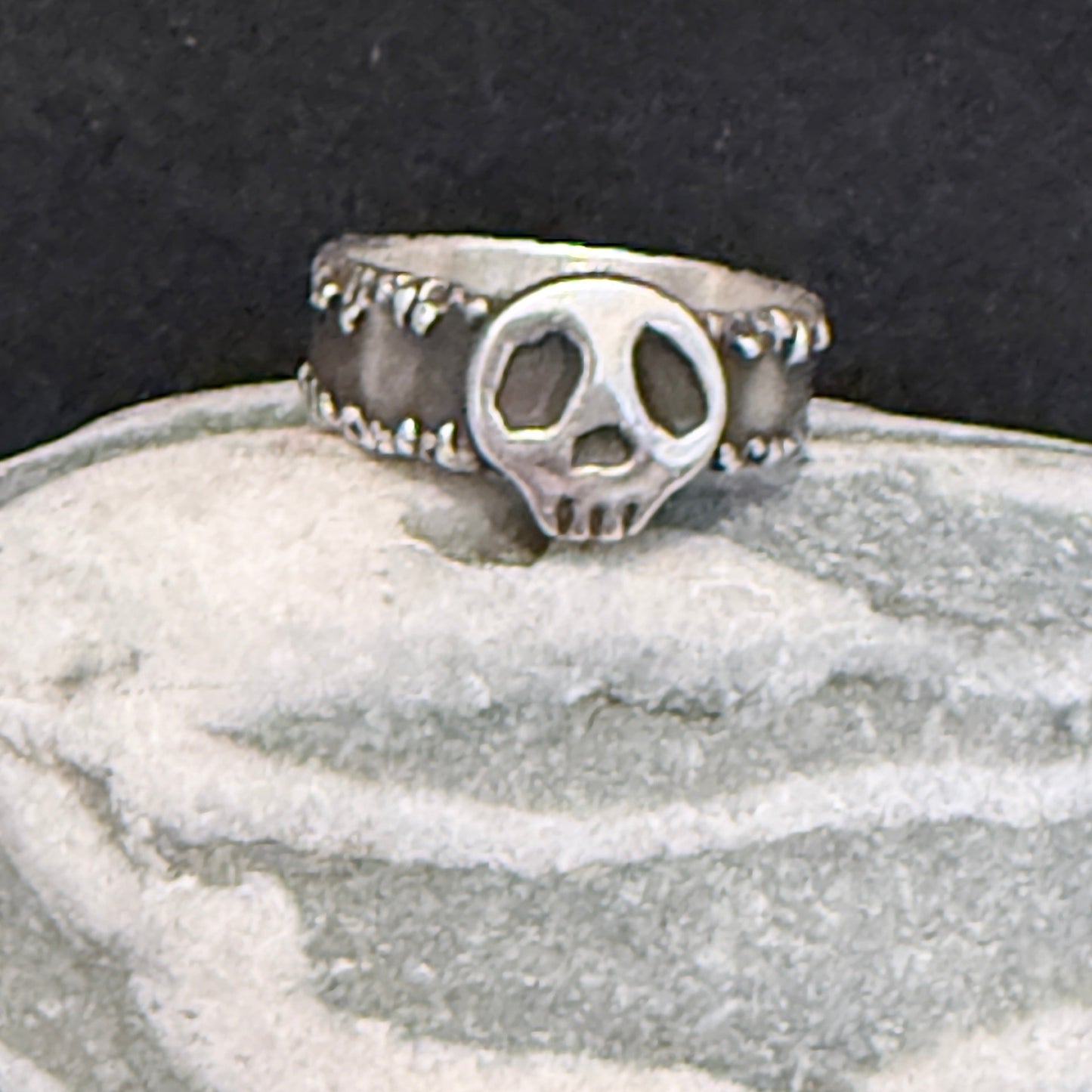 Silver ring with a skull design on a textured surface