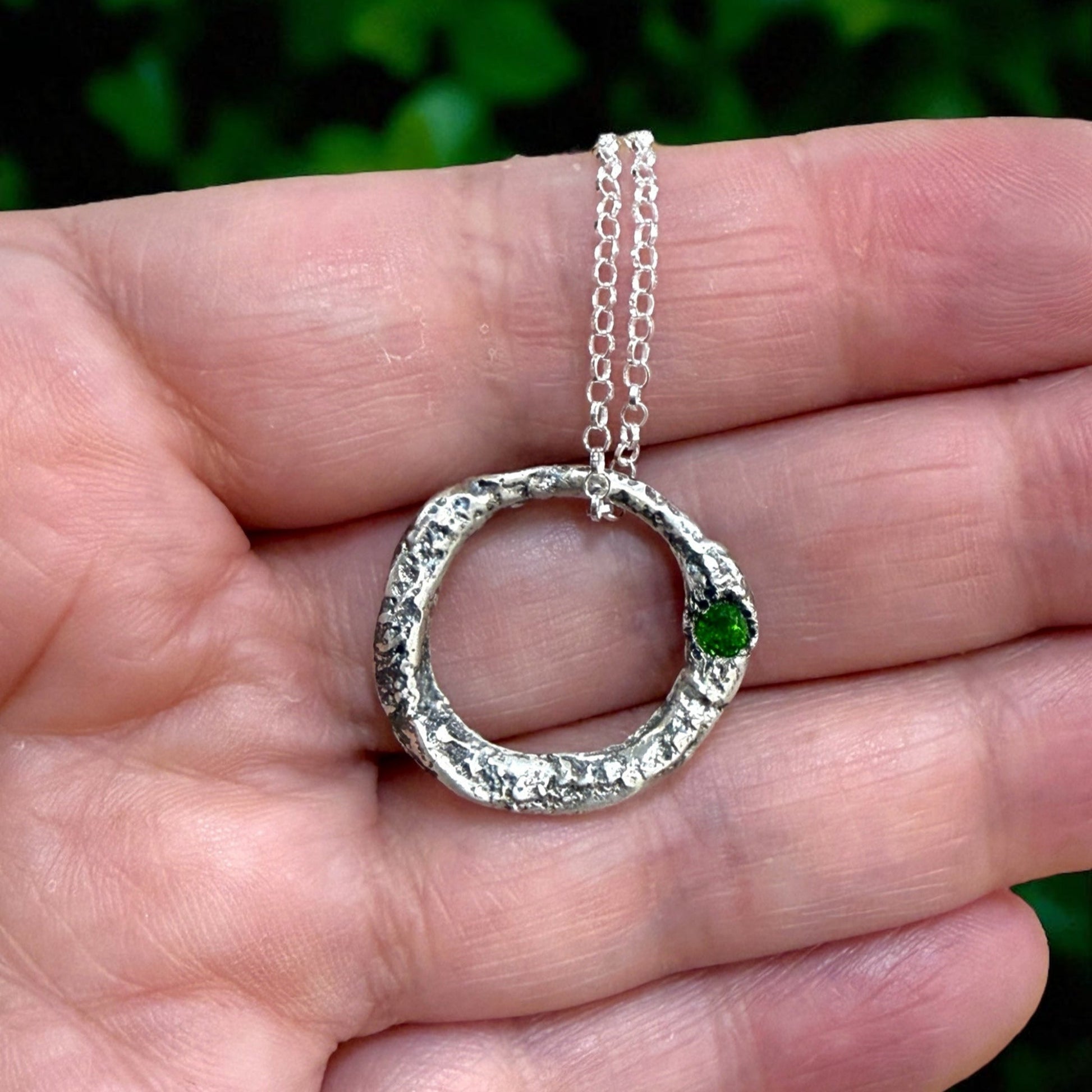 Silver necklace with a green gemstone held in a hand against a blurred green background