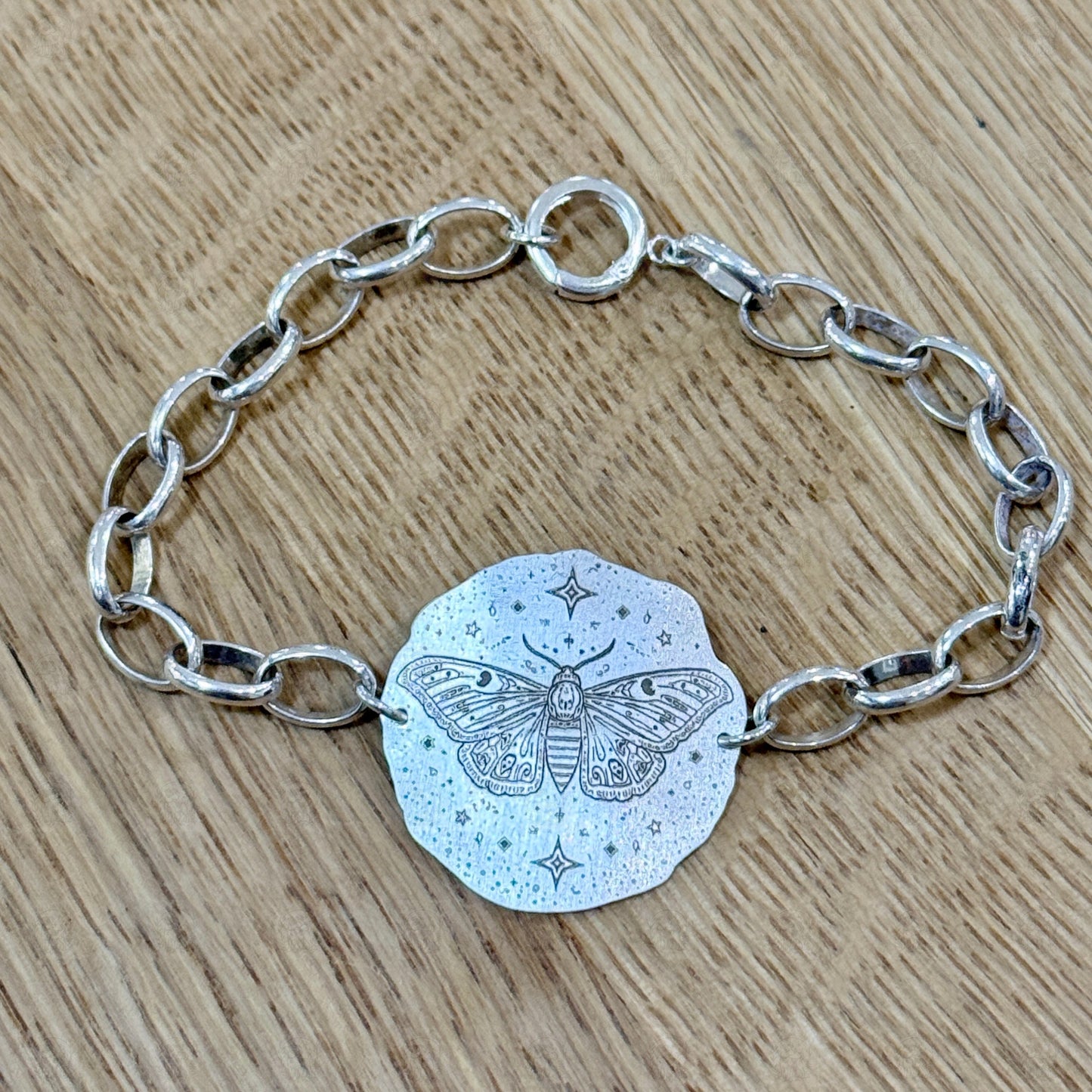 A bracelet with a deaths head moth design on a wooden background.
