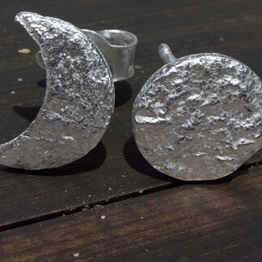 Silver crescent moon and round textured earrings on a dark wooden surface