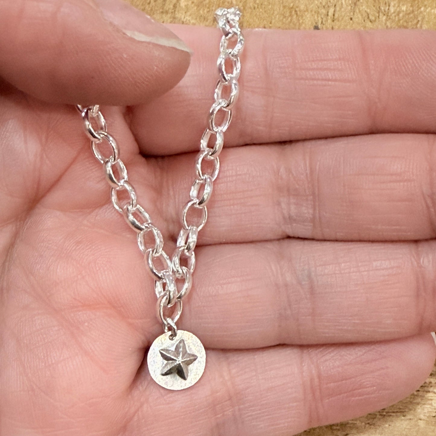 Silver bracelet with a star charm held in a hand on a wooden surface