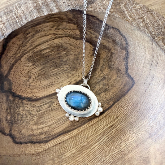 A sterling silver and labradorite pendant on a wooden background