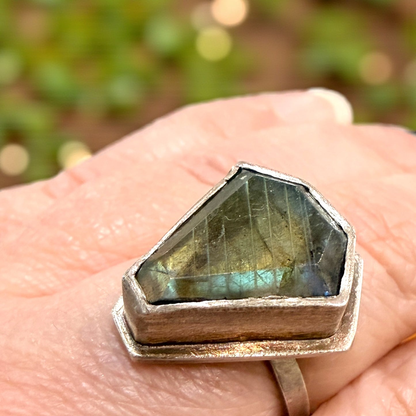 Labradorite ring with silver setting on a hand against a blurred natural background