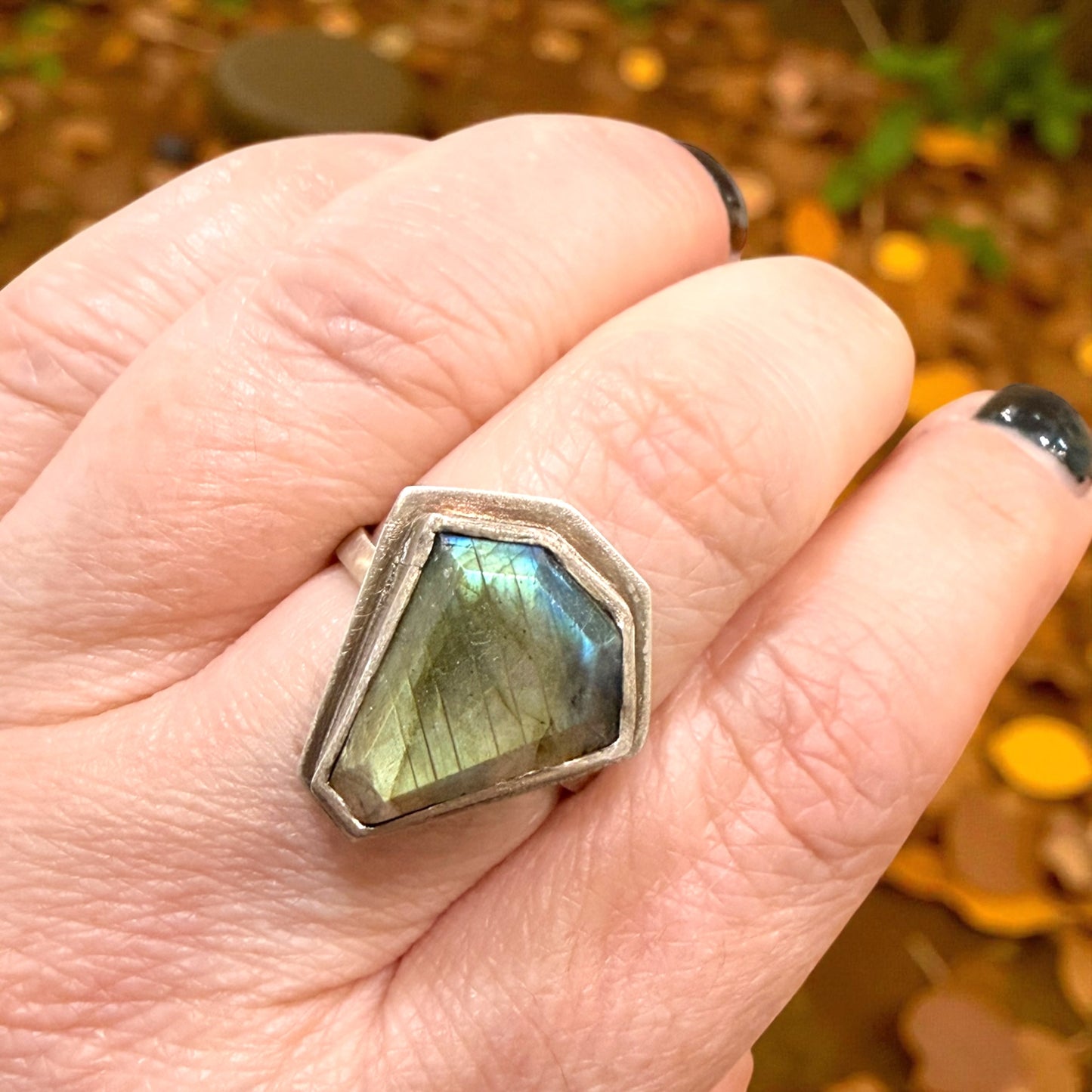 Hand wearing a ring with a Labradorite stone against a natural background