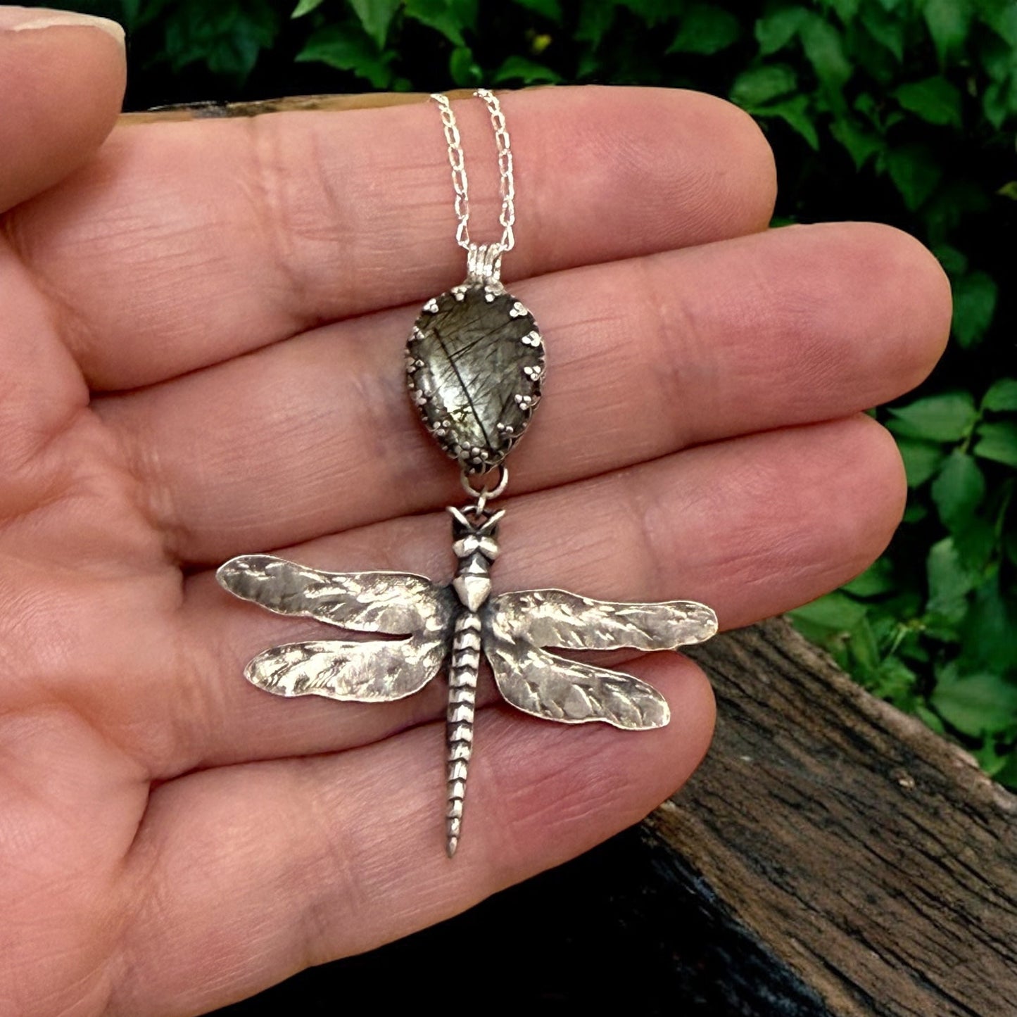 Silver dragonfly pendant necklace held in a hand with a natural background