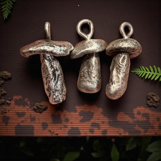 Three silver  mushroom-shaped pendants on a dark brown surface with green leaves.