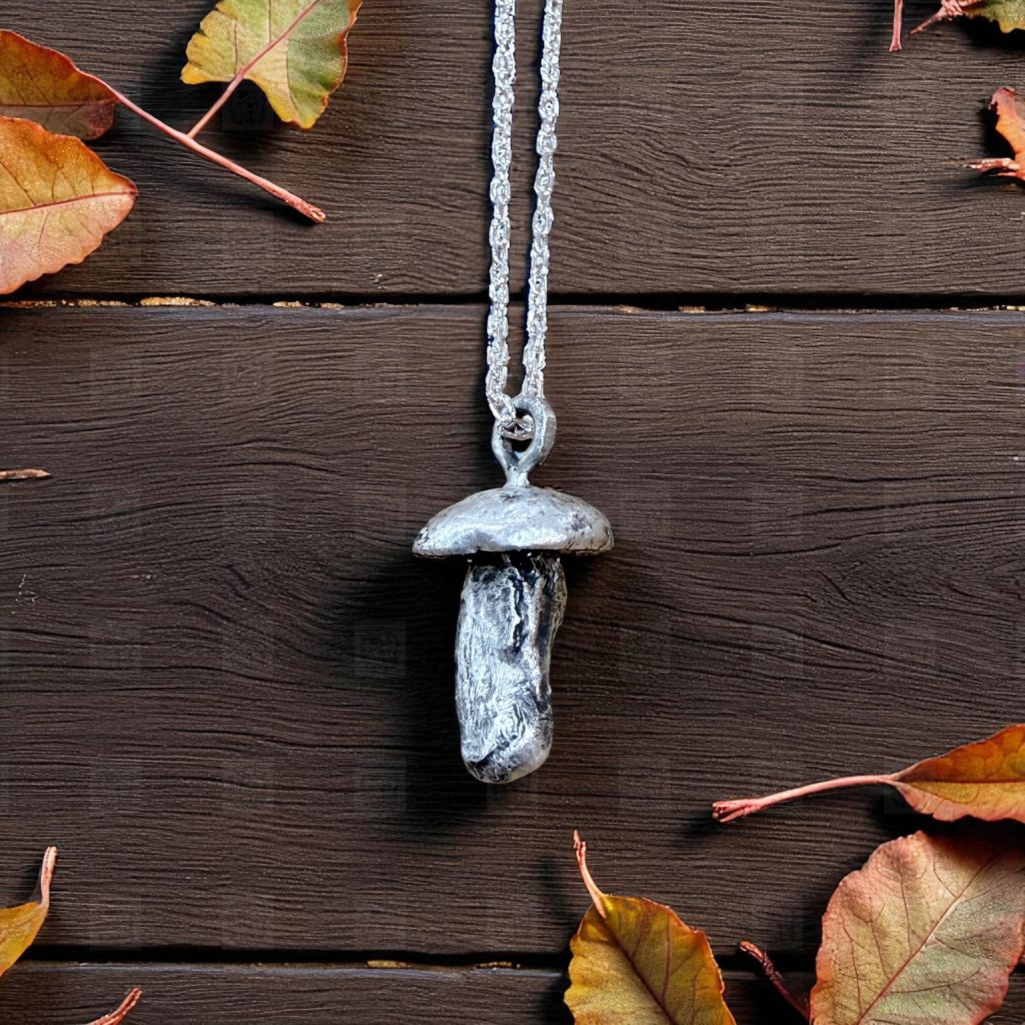 Mushroom-shaped pendant necklace on a wooden surface with autumn leaves