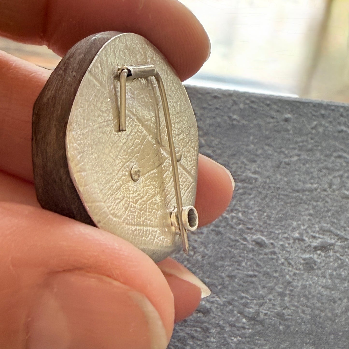 Close-up of a hand holding a textured silver brooch with a blurred background