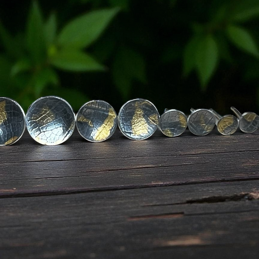 Silver earrings arranged on a wooden surface with a dark green leafy background