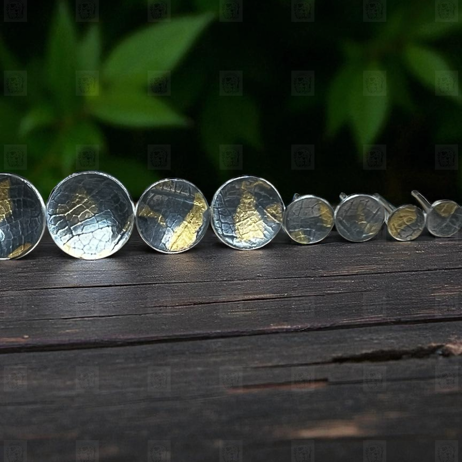 Silver earrings arranged on a wooden surface with a dark green leafy background