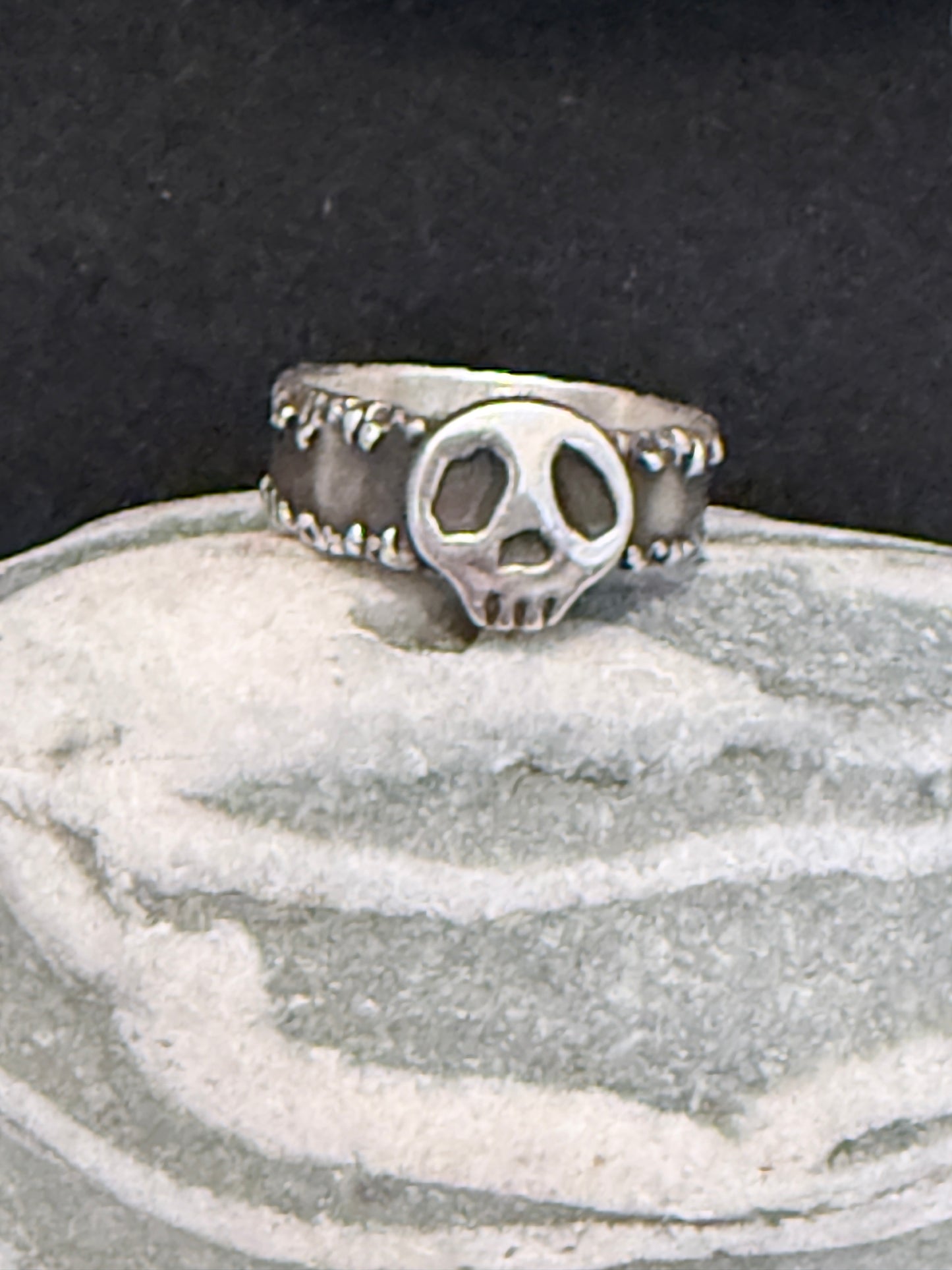 Silver ring with a skull design on a textured surface