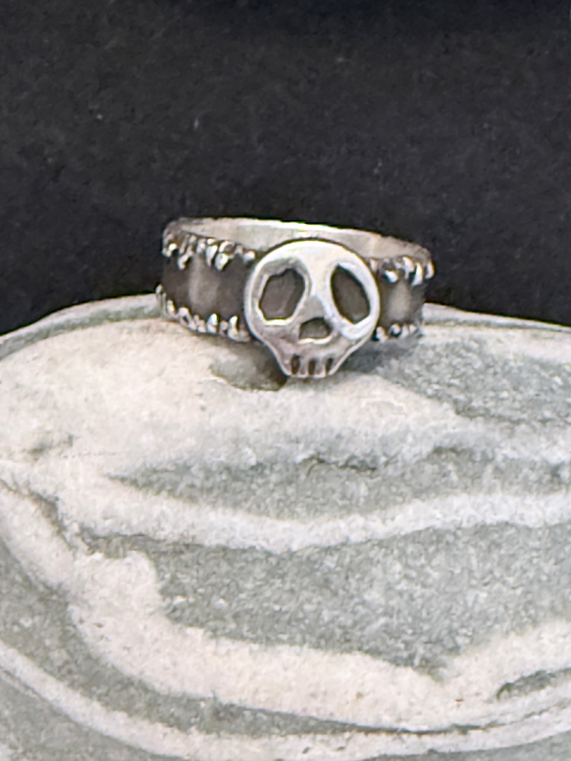 Silver ring with a skull design on a textured surface