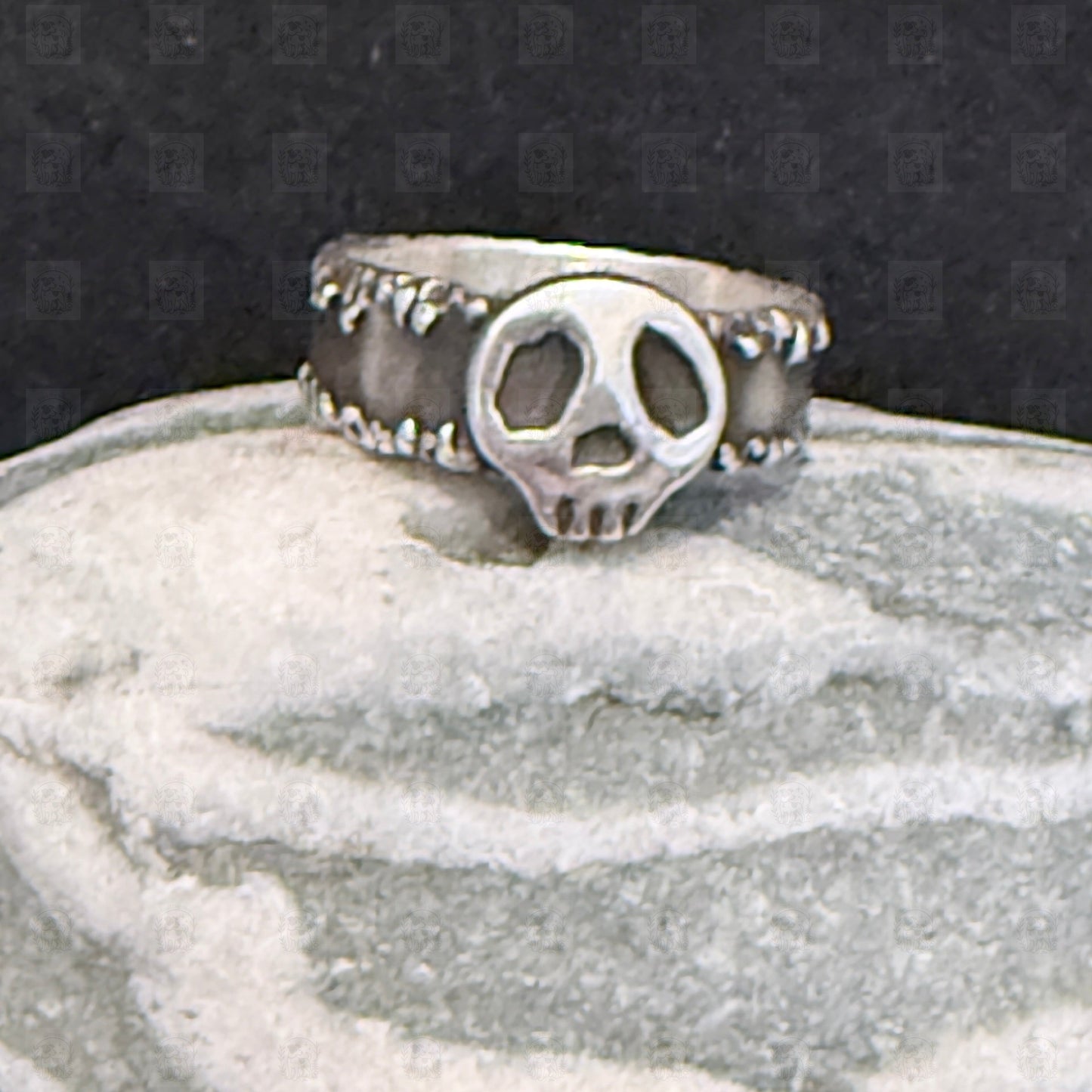 Silver ring with a skull design on a textured surface