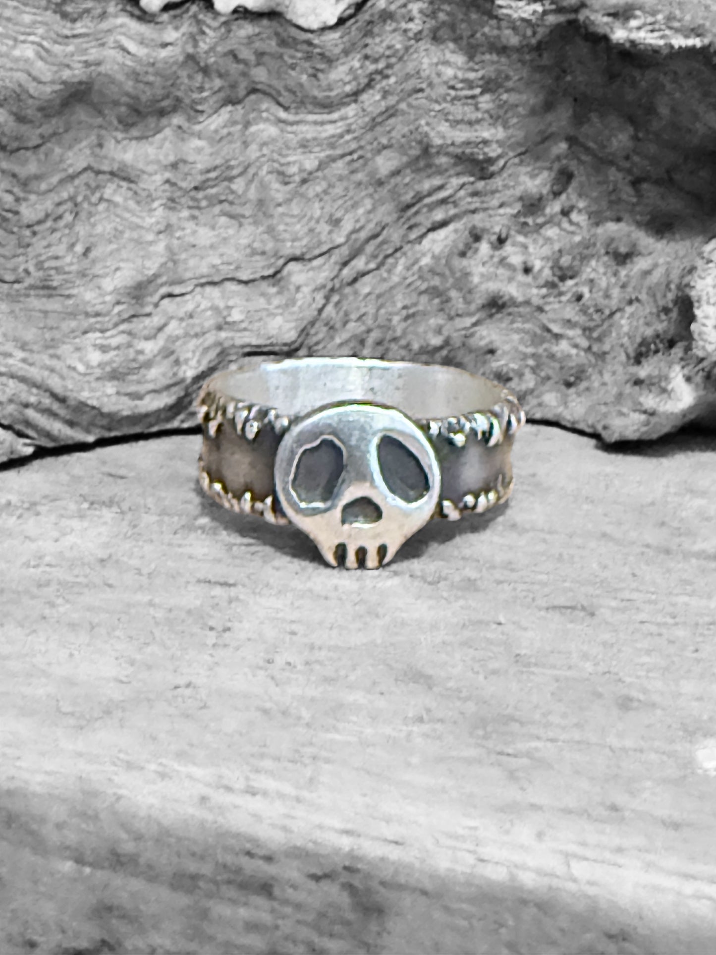 Silver skull ring on a wooden surface with a stone background