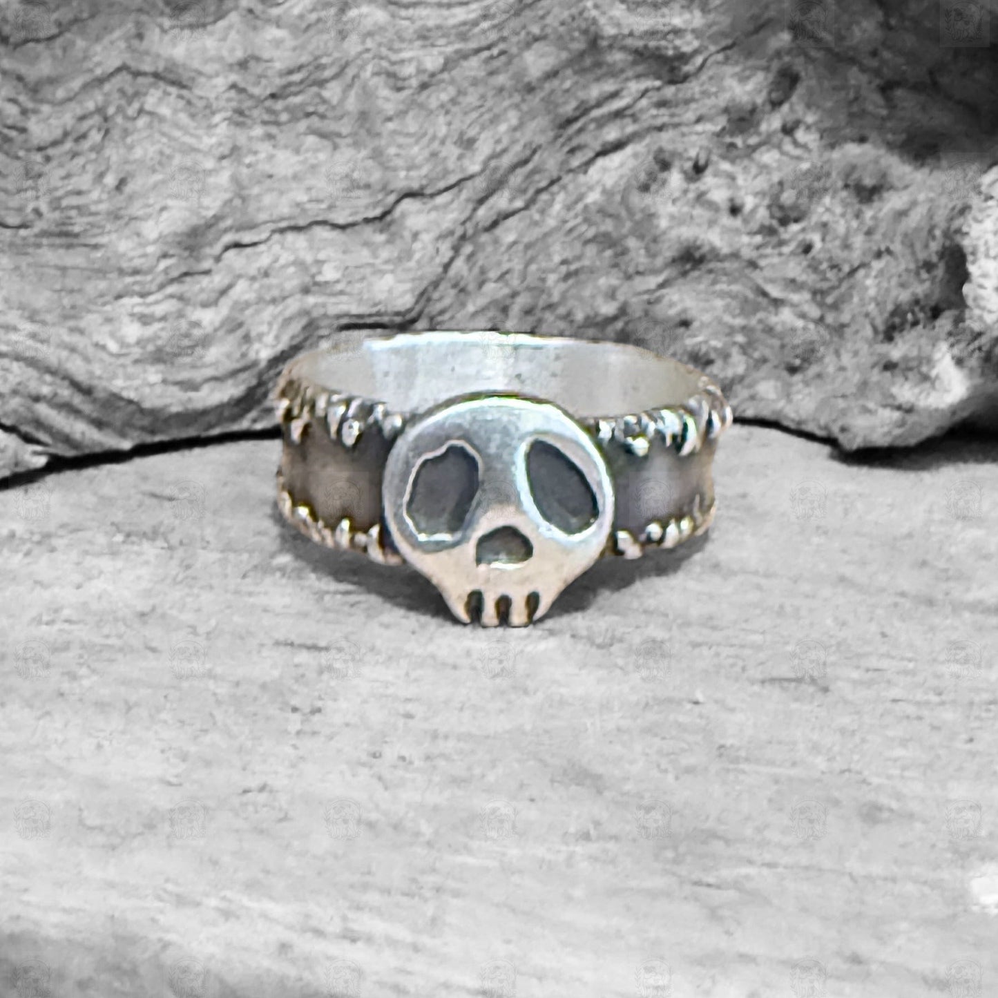Silver skull ring on a wooden surface with a stone background
