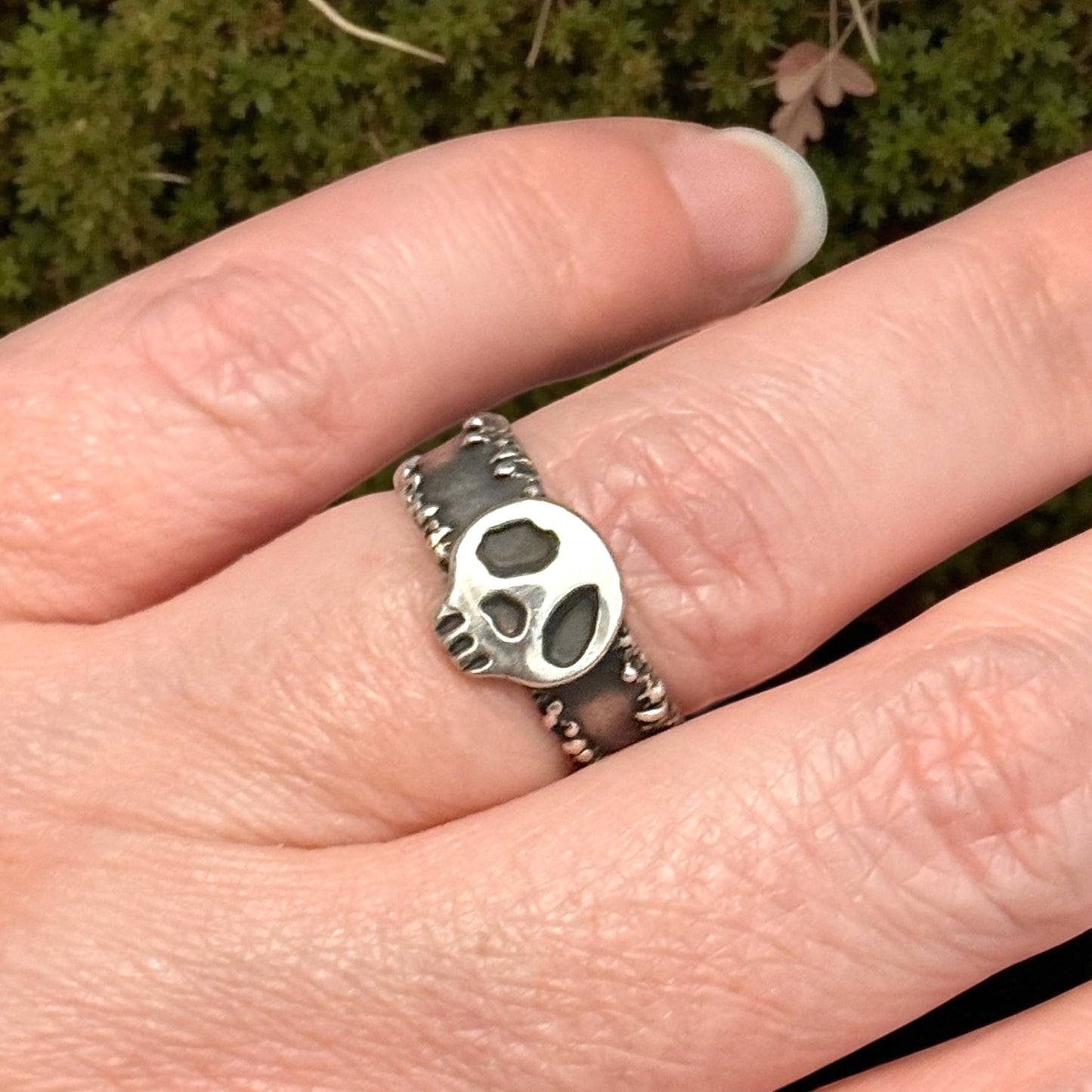 Silver skull ring on a finger with a blurred green background