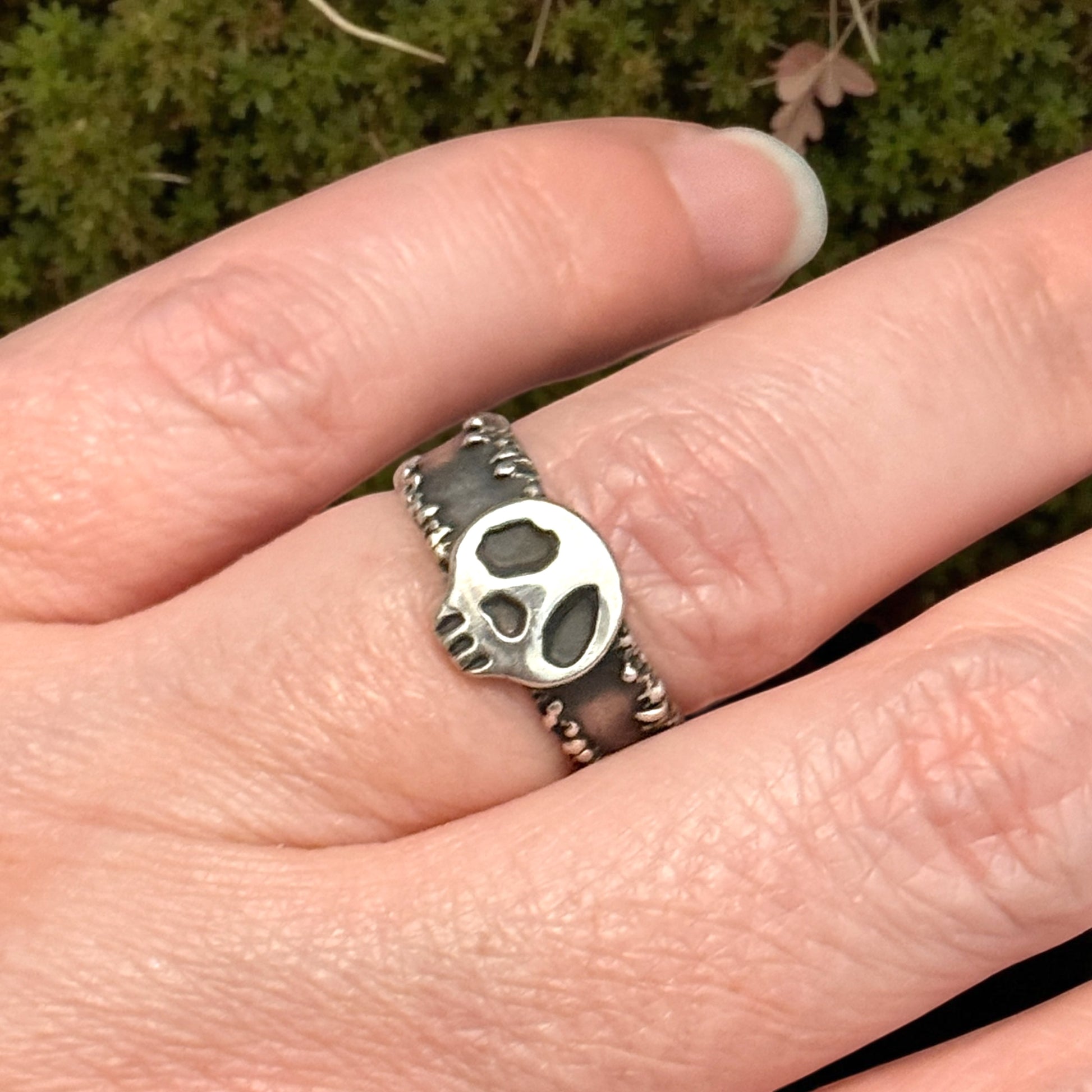 Silver skull ring on a finger with a blurred green background