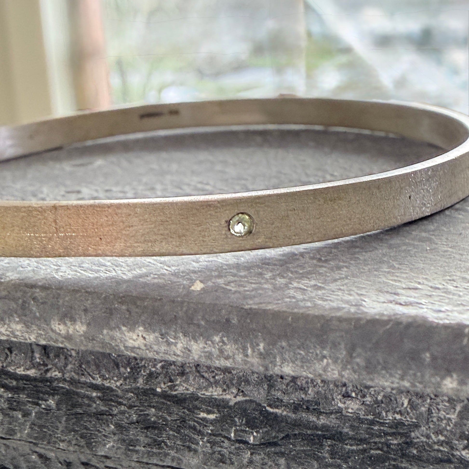 Silver bracelet with a small peridot on a stone surface