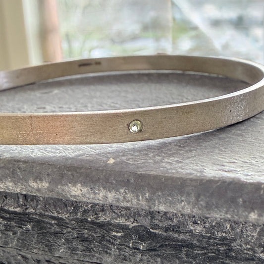 Silver bracelet with a small peridot on a stone surface