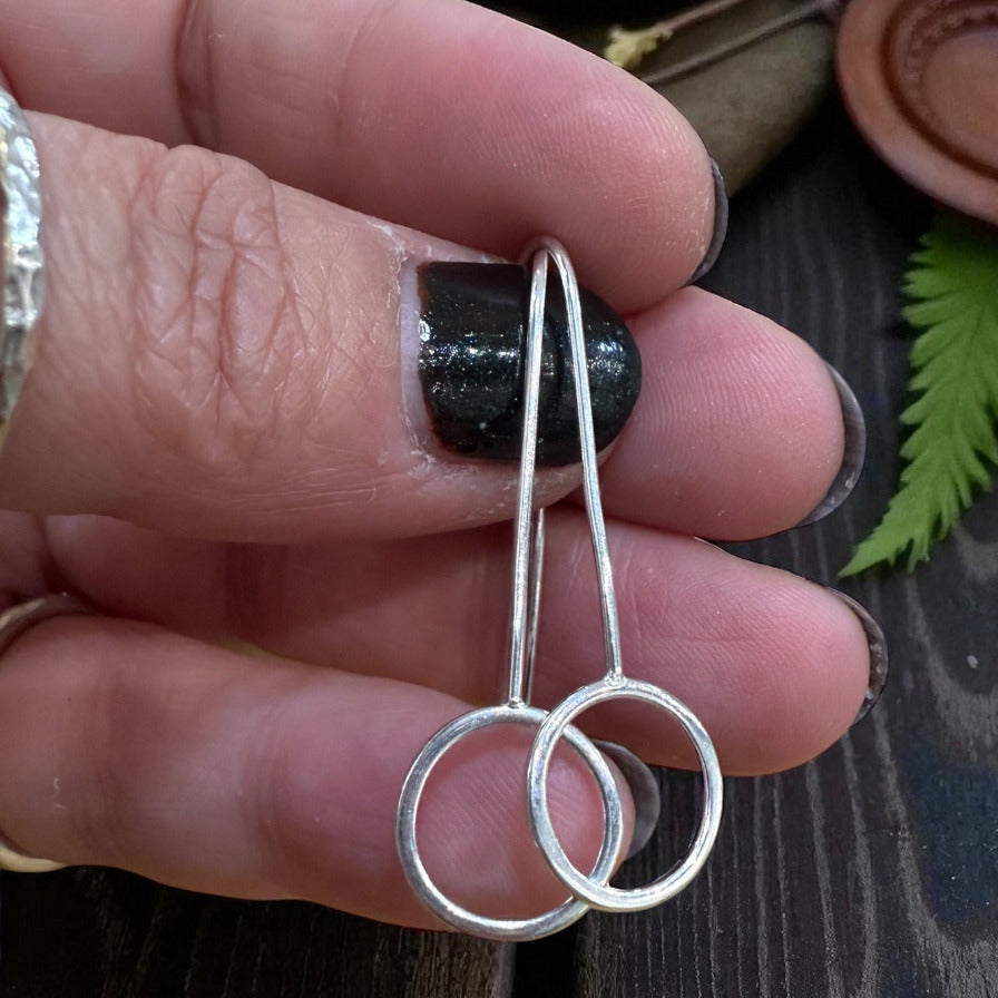 Silver earrings held between fingers on a wooden surface