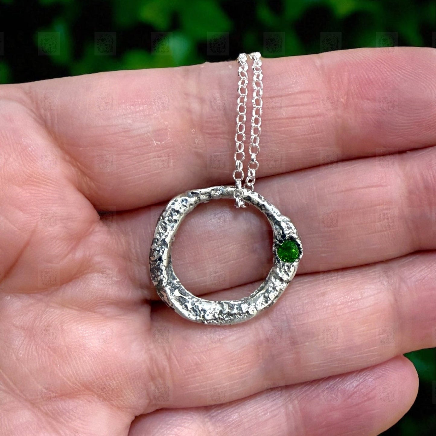 Silver necklace with a green gemstone held in a hand against a blurred green background