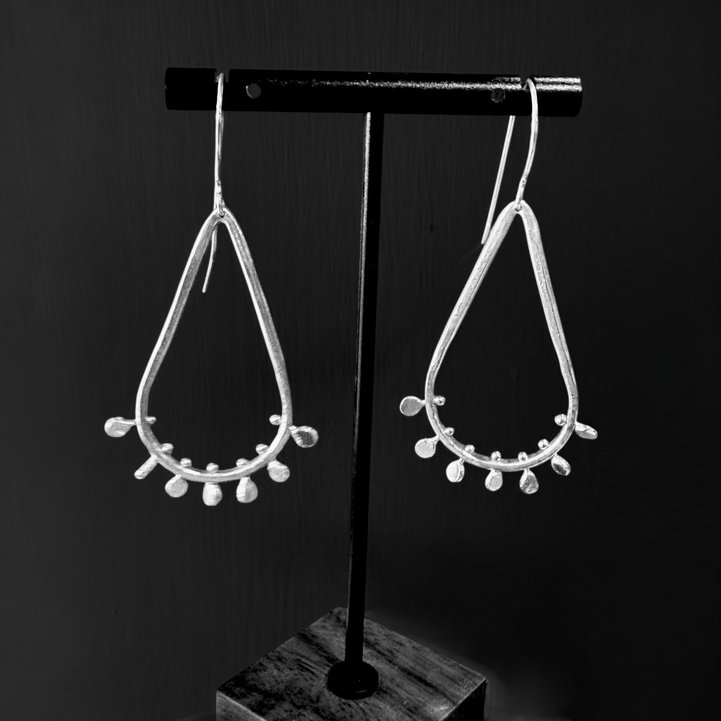 Pair of silver teardrop earrings on a black stand against a dark background