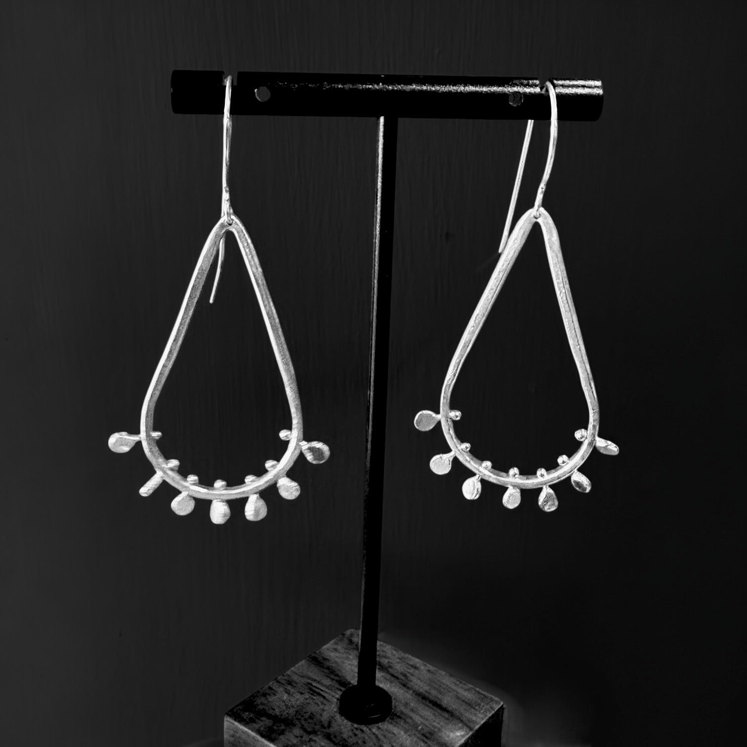 Pair of silver teardrop earrings on a black stand against a dark background