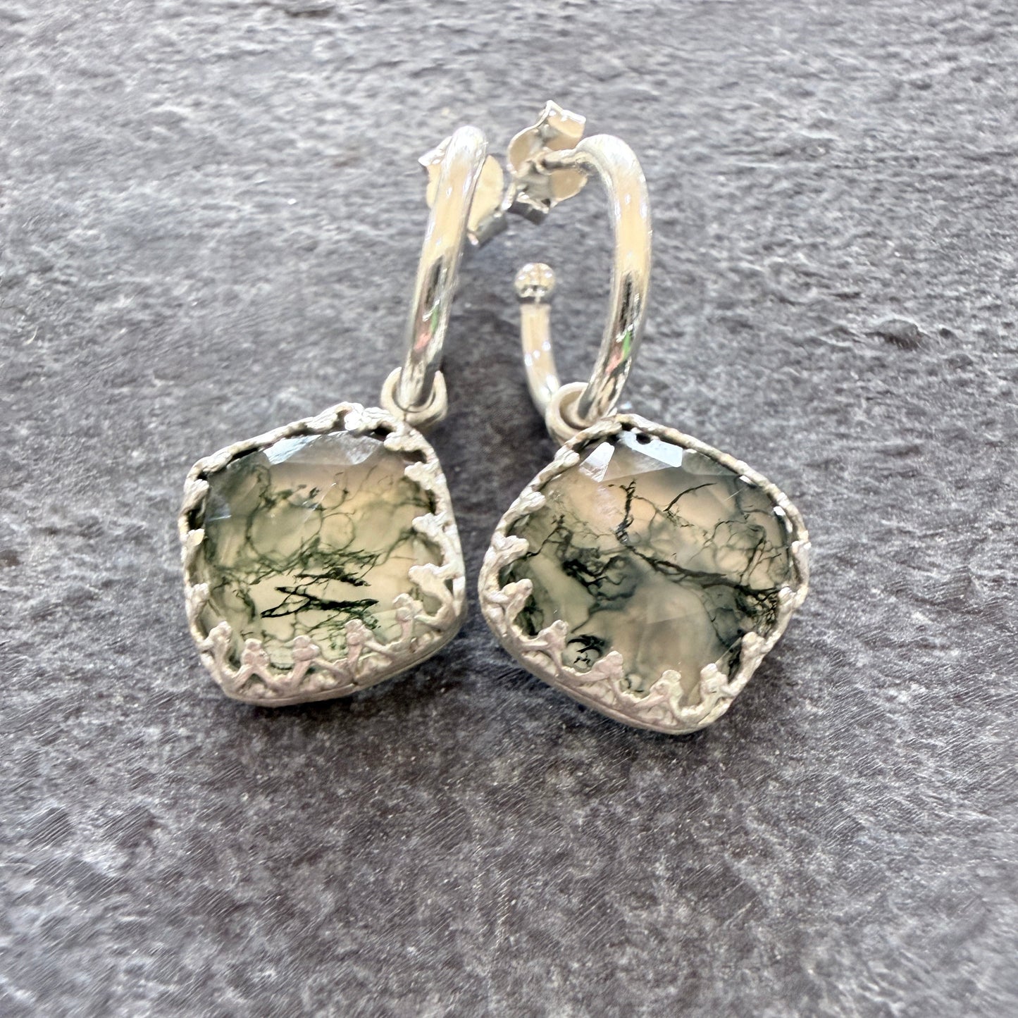Pair of silver earrings with moss agate stones on a slate surface