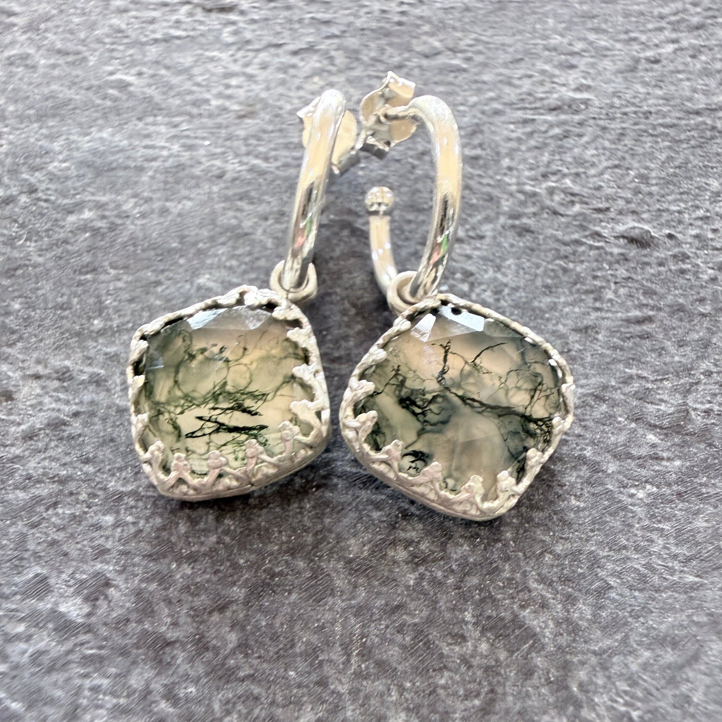 Pair of silver earrings with moss agate stones on a slate surface