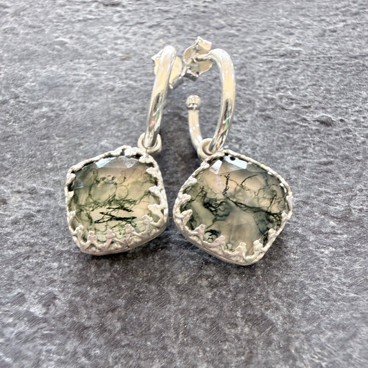 Pair of silver earrings with moss agate stones on a slate surface