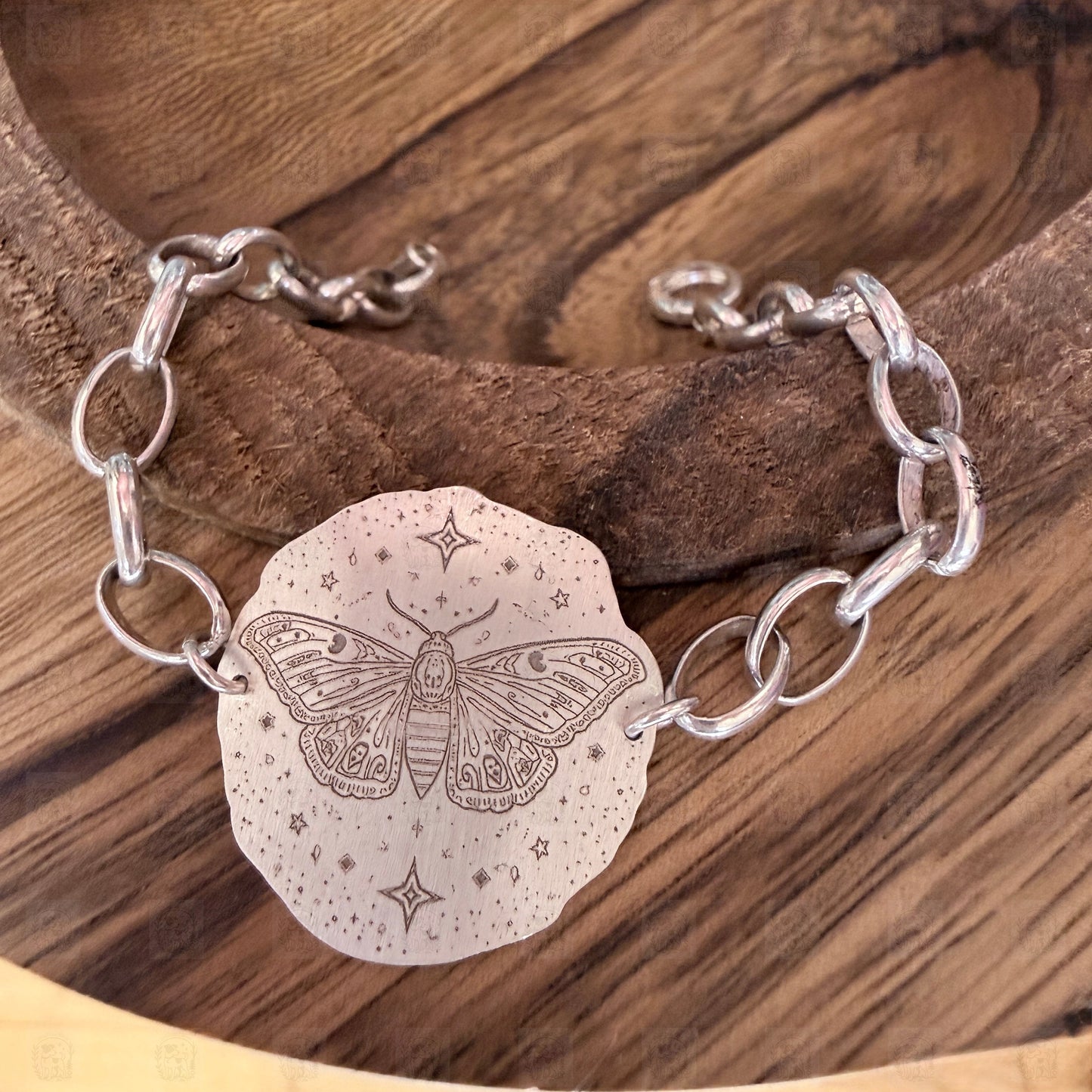 A bracelet with a deaths head moth design on a wooden background.