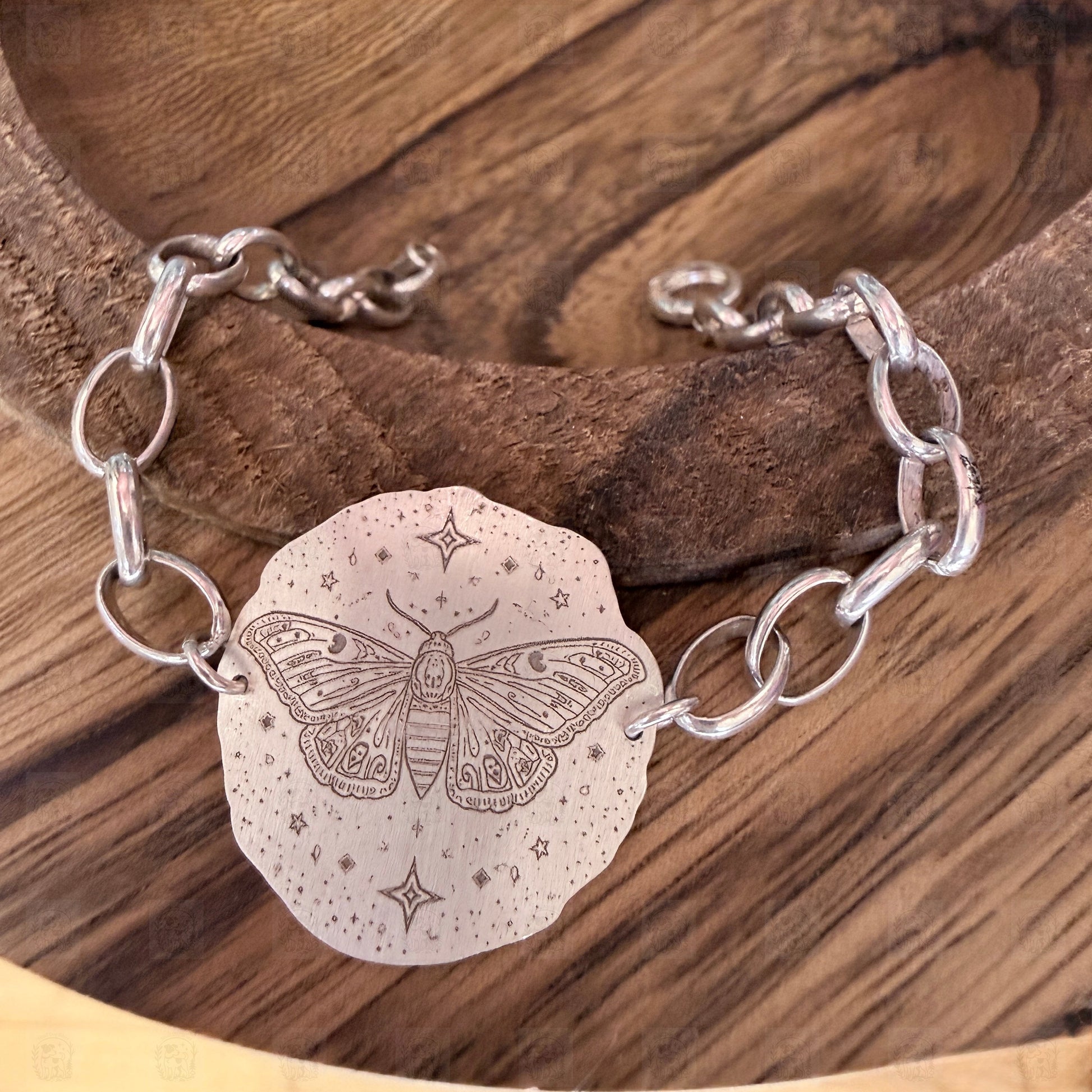 A bracelet with a deaths head moth design on a wooden background.