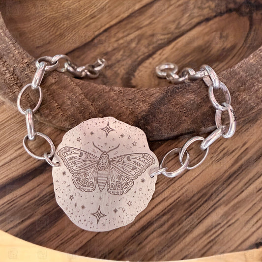 A bracelet with a deaths head moth design on a wooden background.
