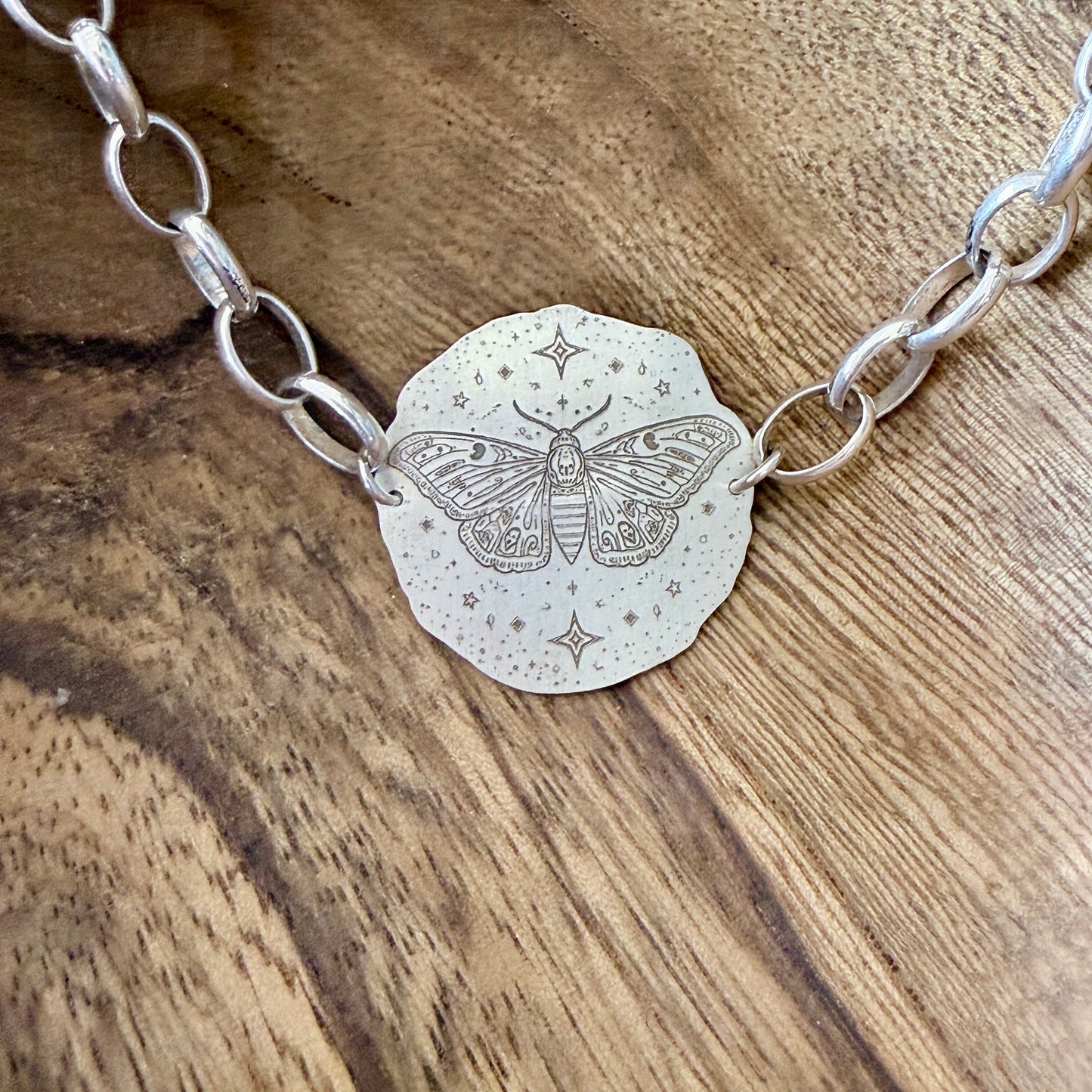 A bracelet with a deaths head moth design on a wooden background.