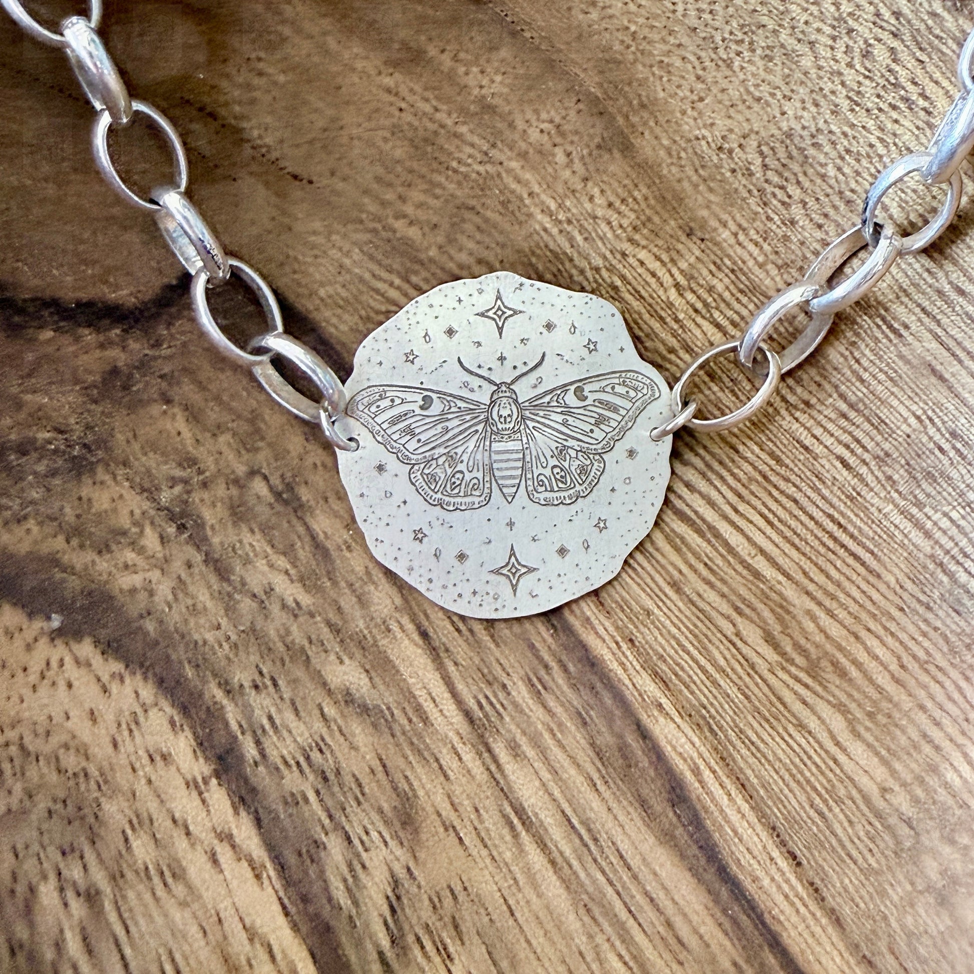 A bracelet with a deaths head moth design on a wooden background.