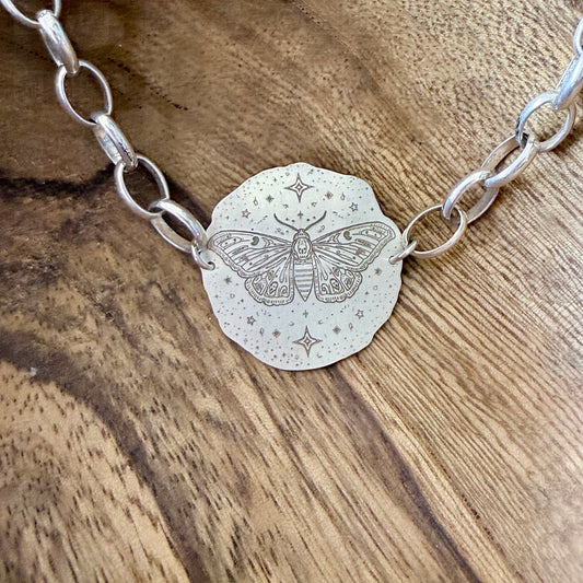 A bracelet with a deaths head moth design on a wooden background.