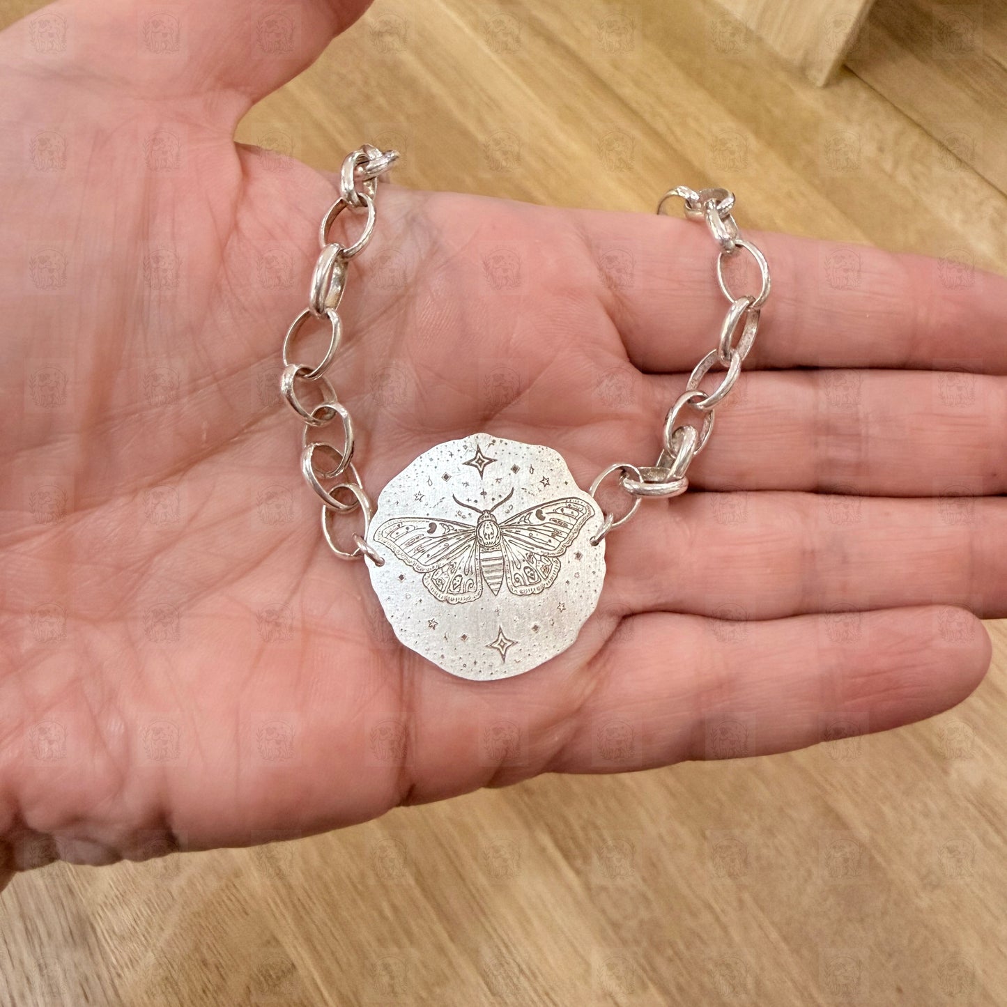 A bracelet with a deaths head moth design on a hand.