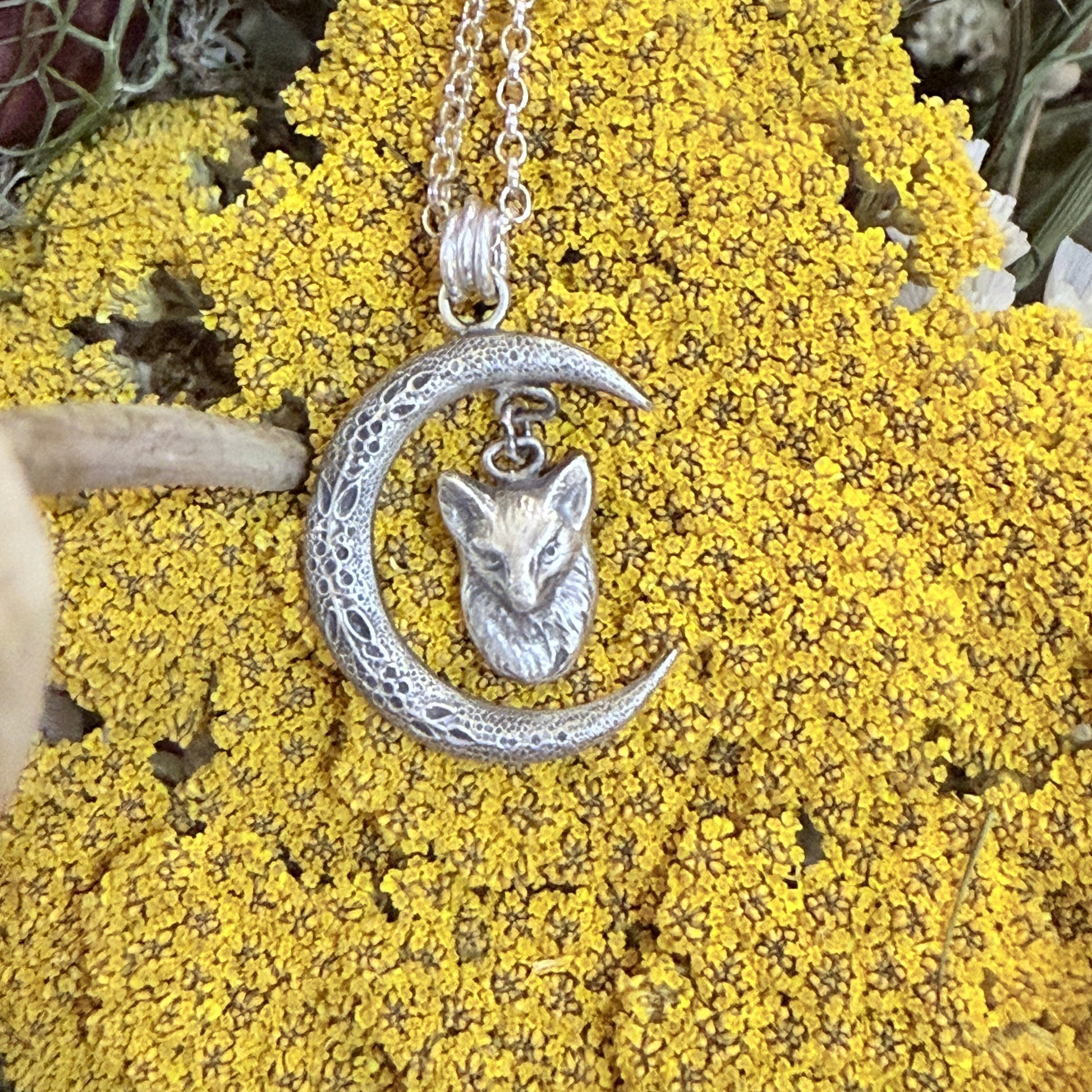 Silver crescent moon and fox pendant on a chain against a yellow floral background