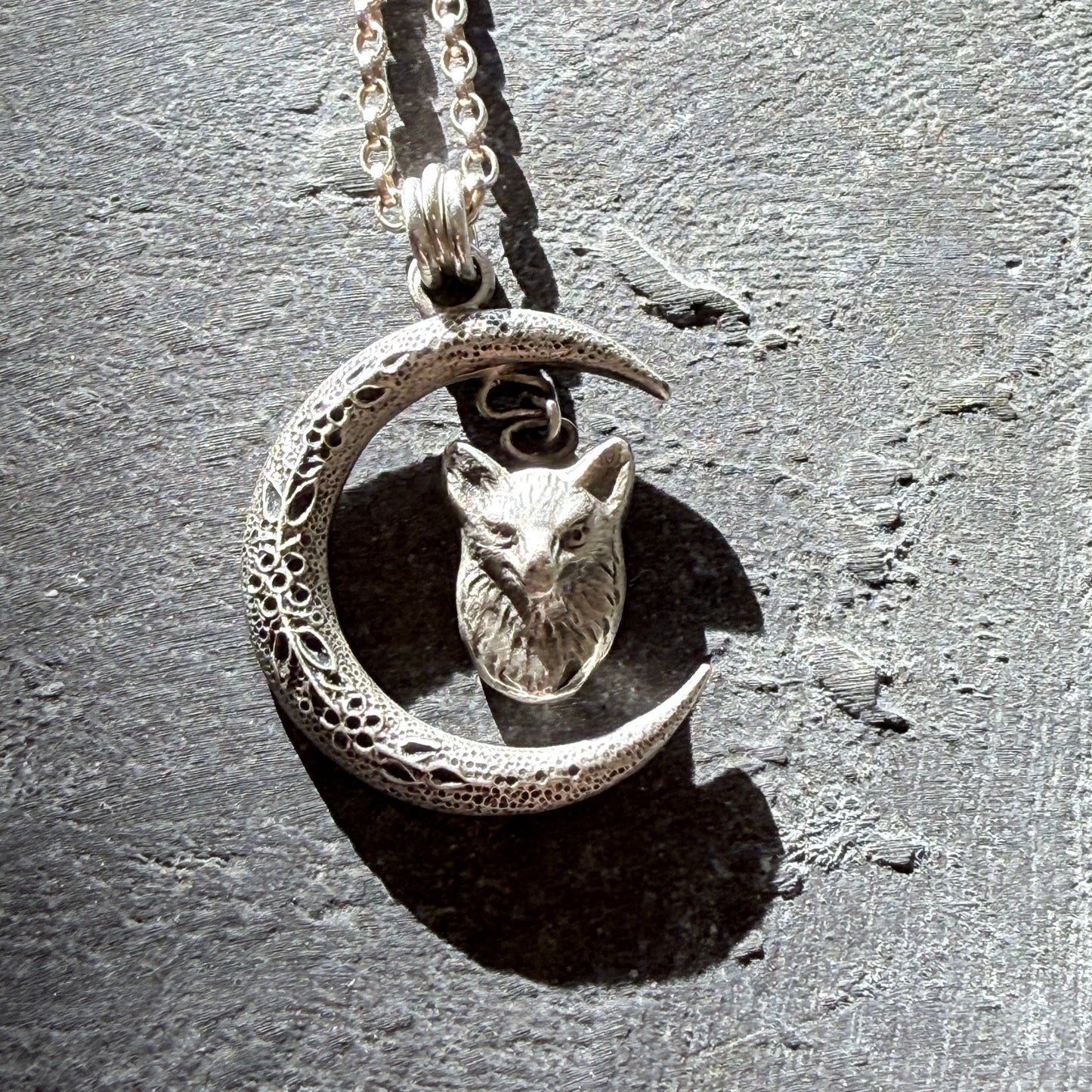 Silver necklace with a crescent moon and fox head pendant on a textured gray background