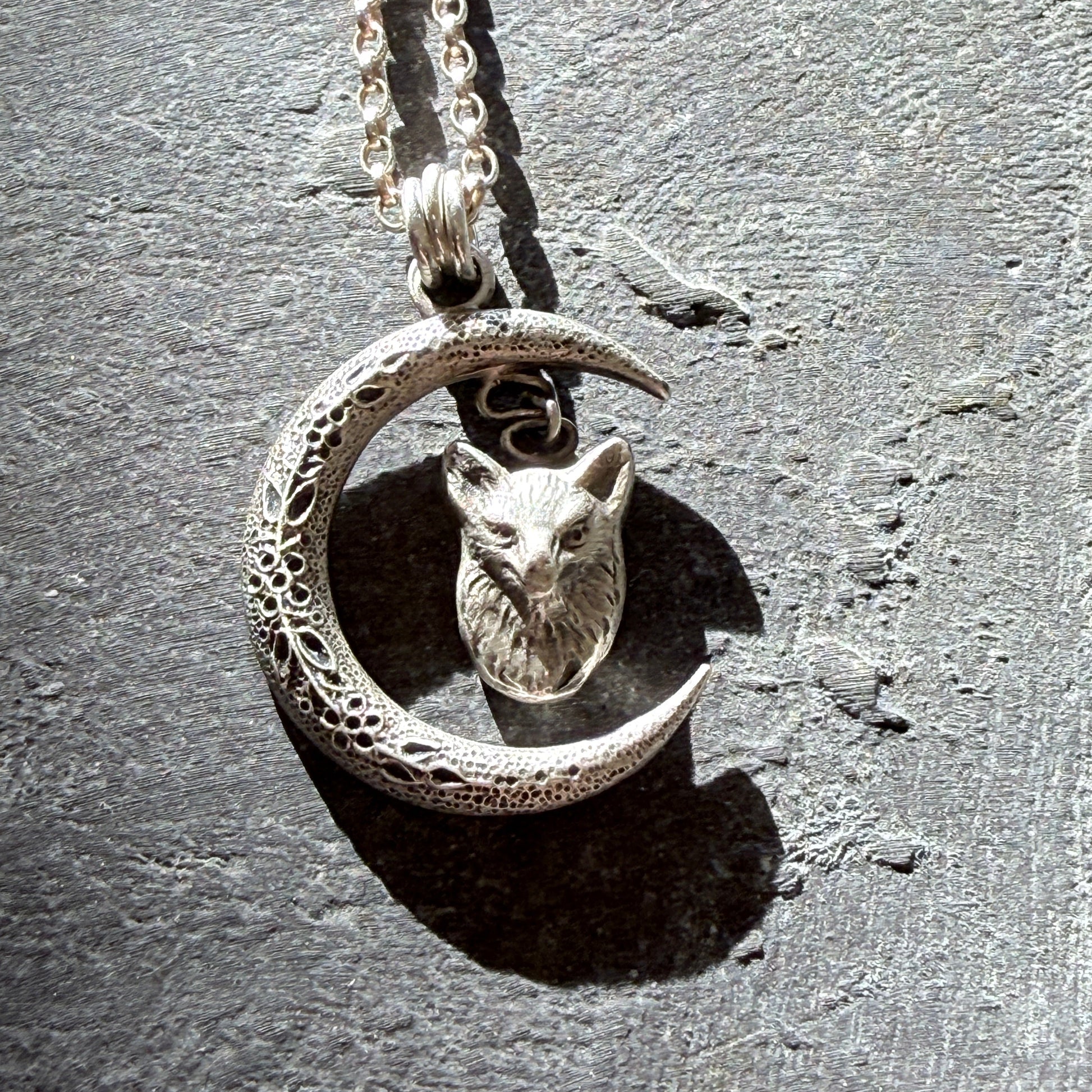Silver necklace with a crescent moon and fox head pendant on a textured gray background