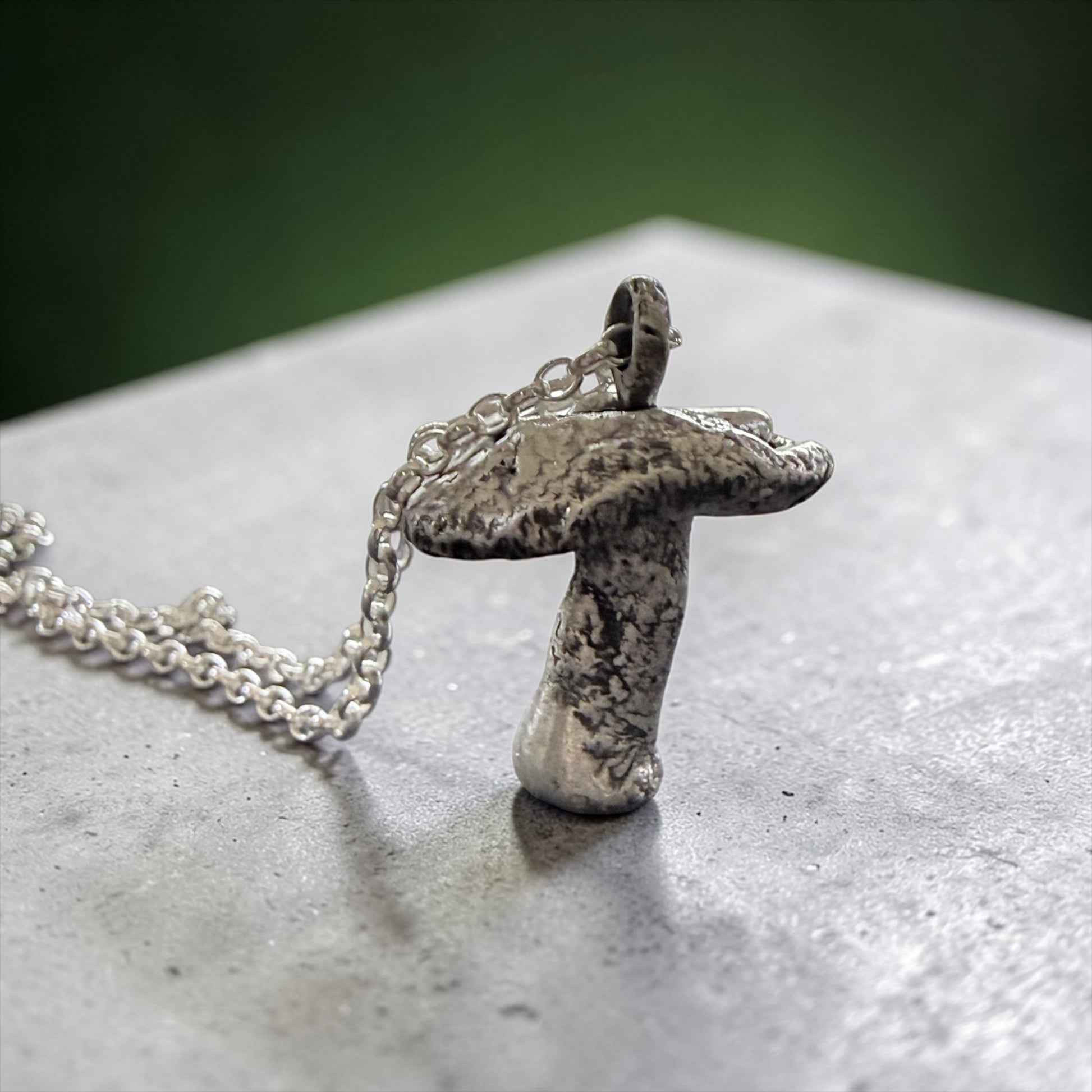 Silver mushroom pendant necklace on a textured surface with a green background