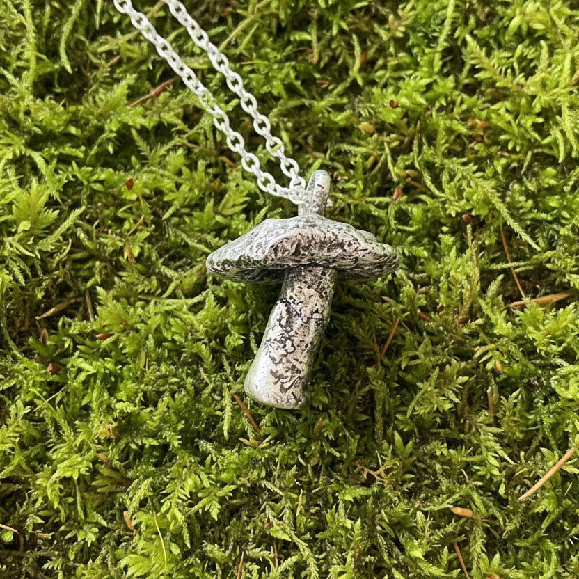 Silver mushroom necklace with a textured pendant on a gray surface