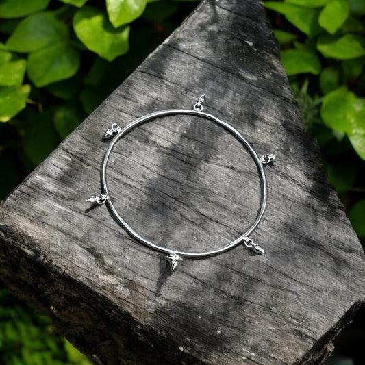 a sterling silver bangle sits on a wooden surface surrounded by greenery.