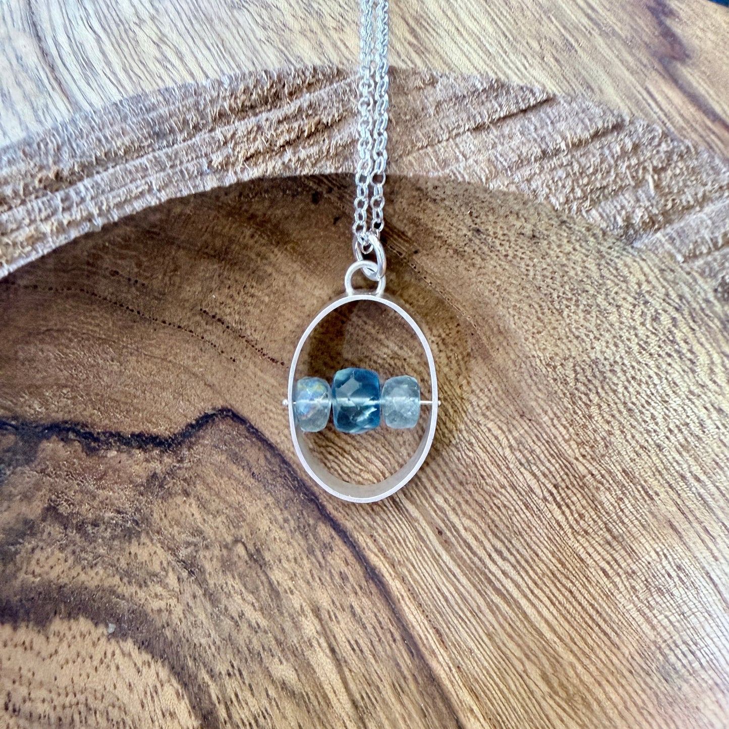 A sterling silver and aquamarine pendant on a wooden background