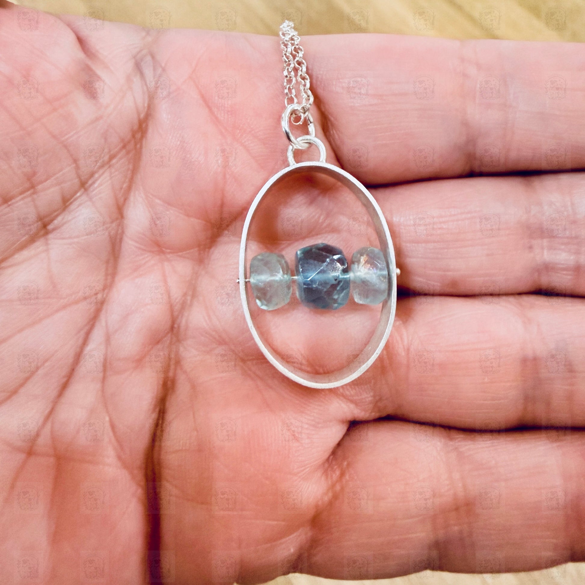 A sterling silver and aquamarine pendant held in a hand.