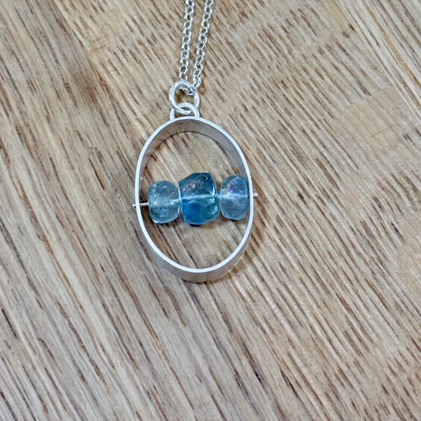 A sterling silver and aquamarine pendant on a wooden background
