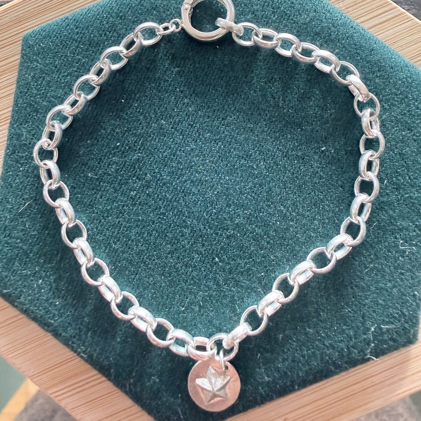 Silver chain bracelet with a star charm on a green cushion