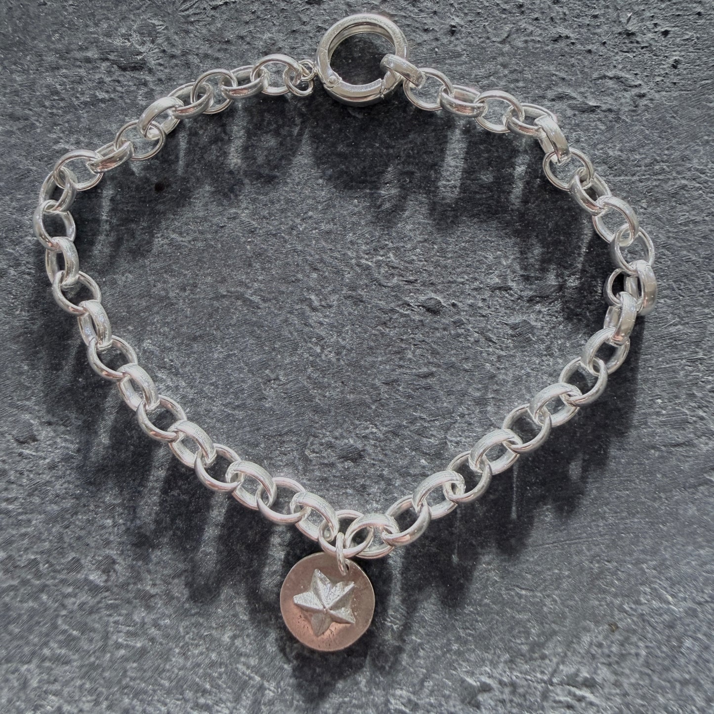 Silver chain bracelet with a star charm on a dark stone surface